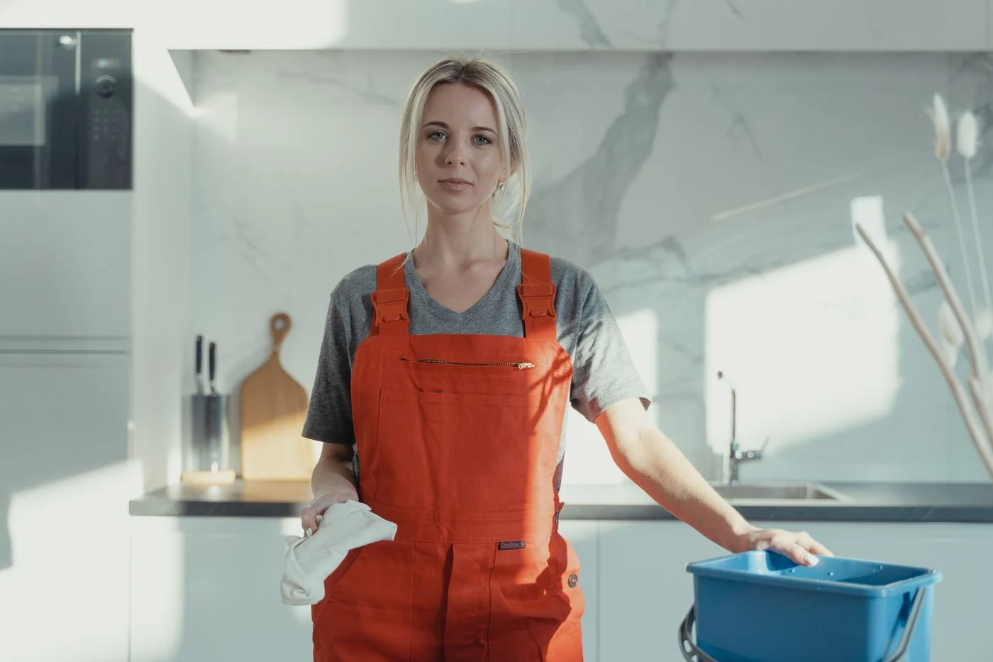 Cleaner holding a cloth beside a bucket in a modern kitchen. — illustrative photograph.